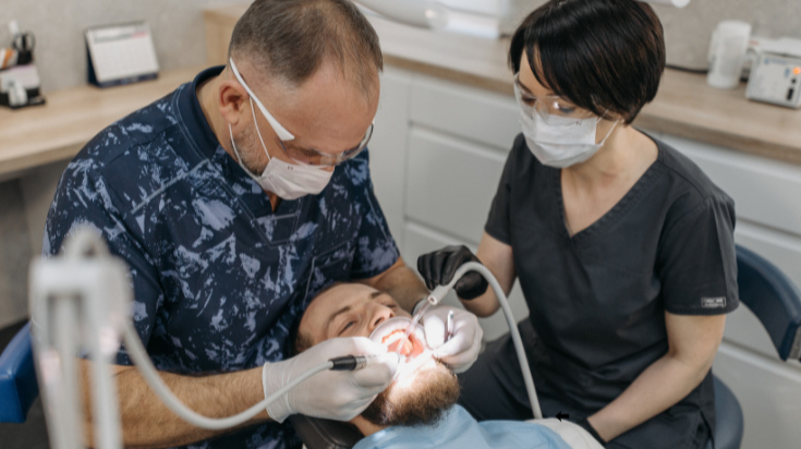 Two dental professionals wearing masks examine a child’s teeth during a dental appointment.