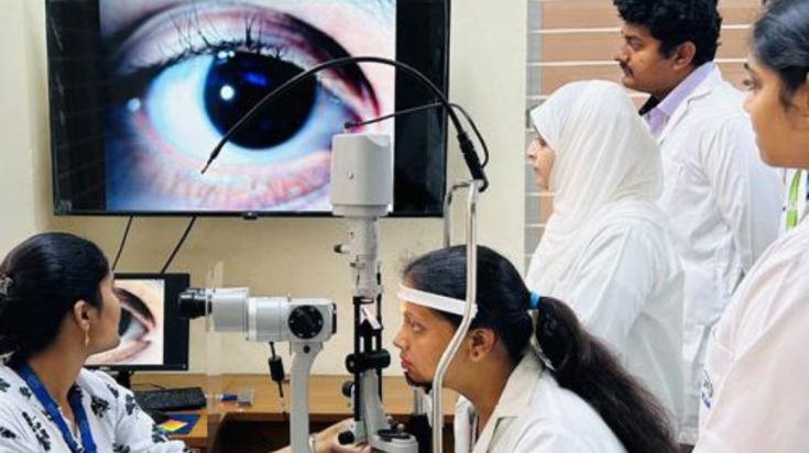 Medical students and healthcare professionals observe an eye examination demonstration displayed on a large monitor in a clinical training setting.